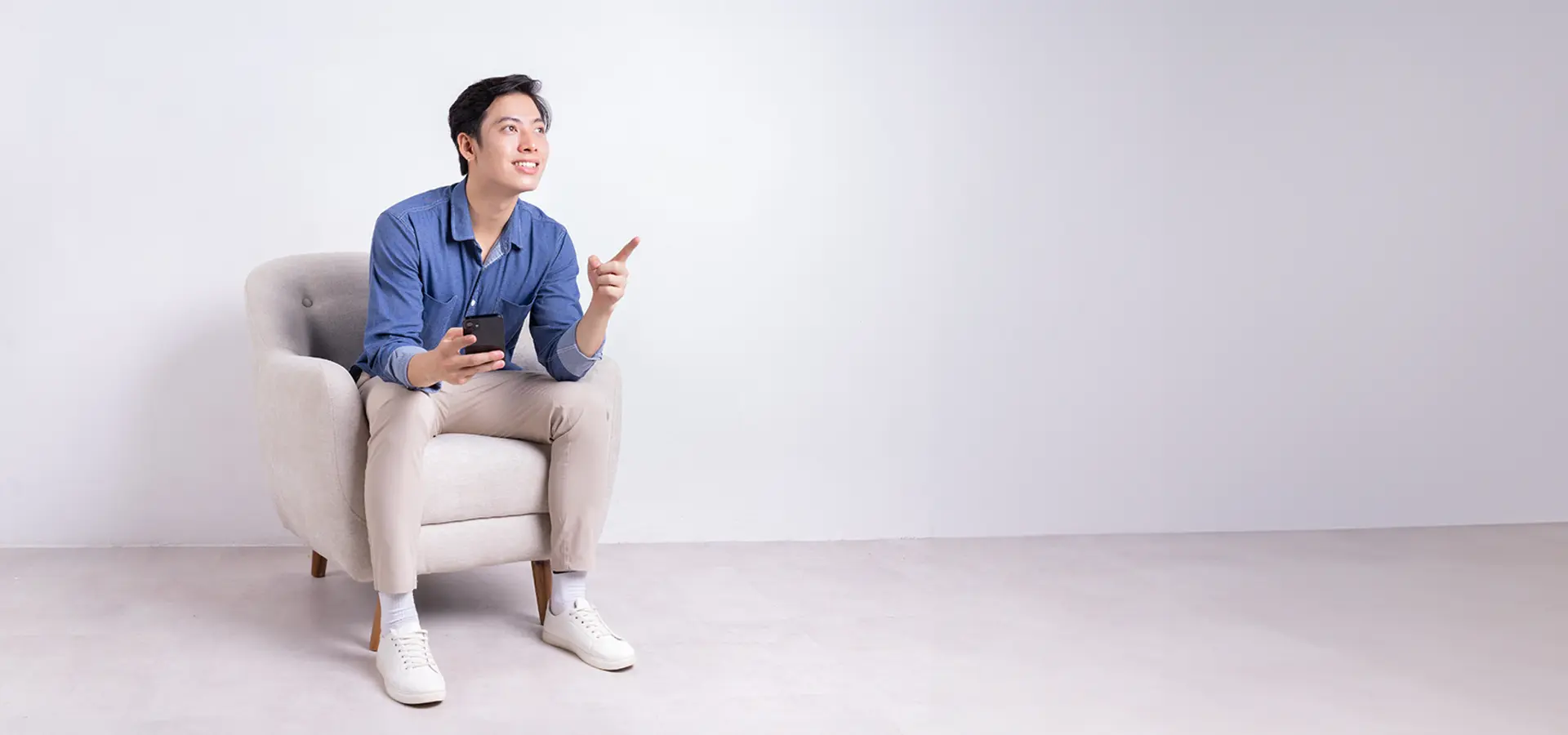 A young man sitting on a couch and holding a cellphone.